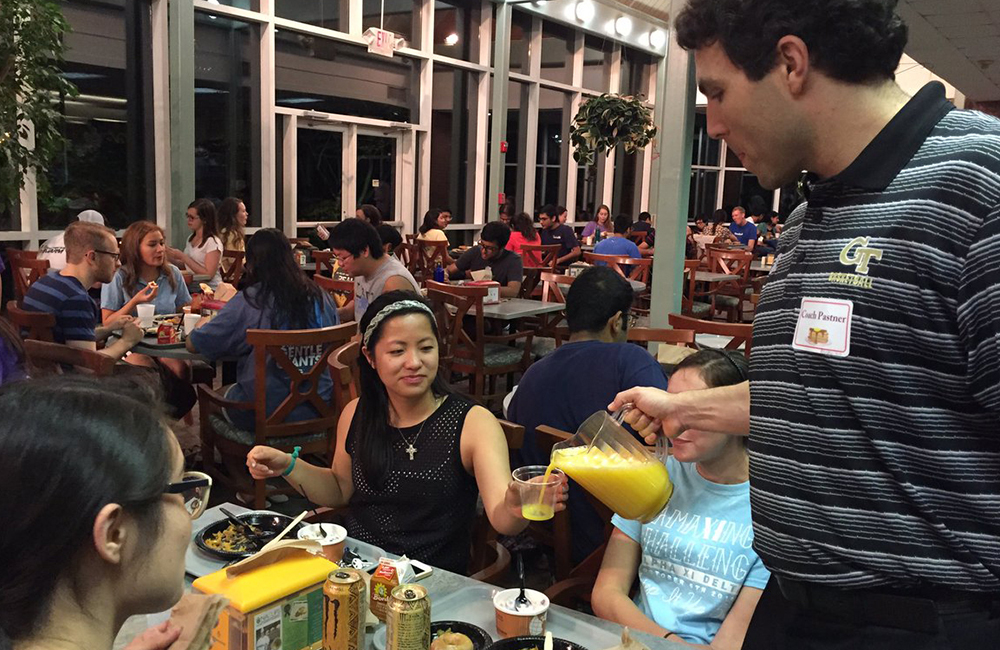 Midnight breakfast, where Josh Pastner, basketball coach, is serving orange juice to students seated at a table