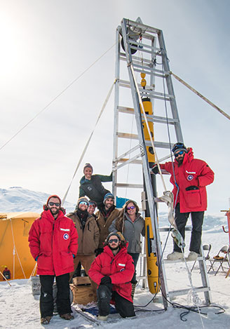 The icefin team standing with icefin hoisted vertically in the air