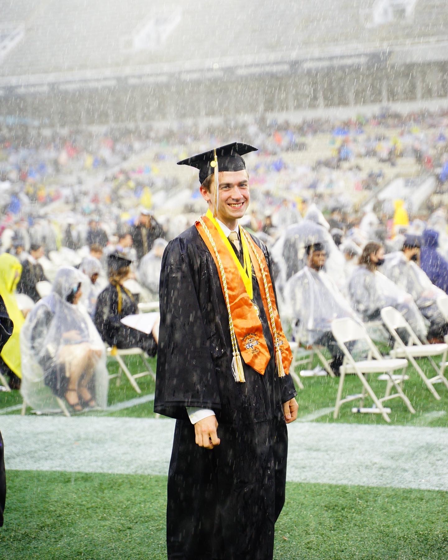 Graduate smiling while standing in the rain at commencement. 
