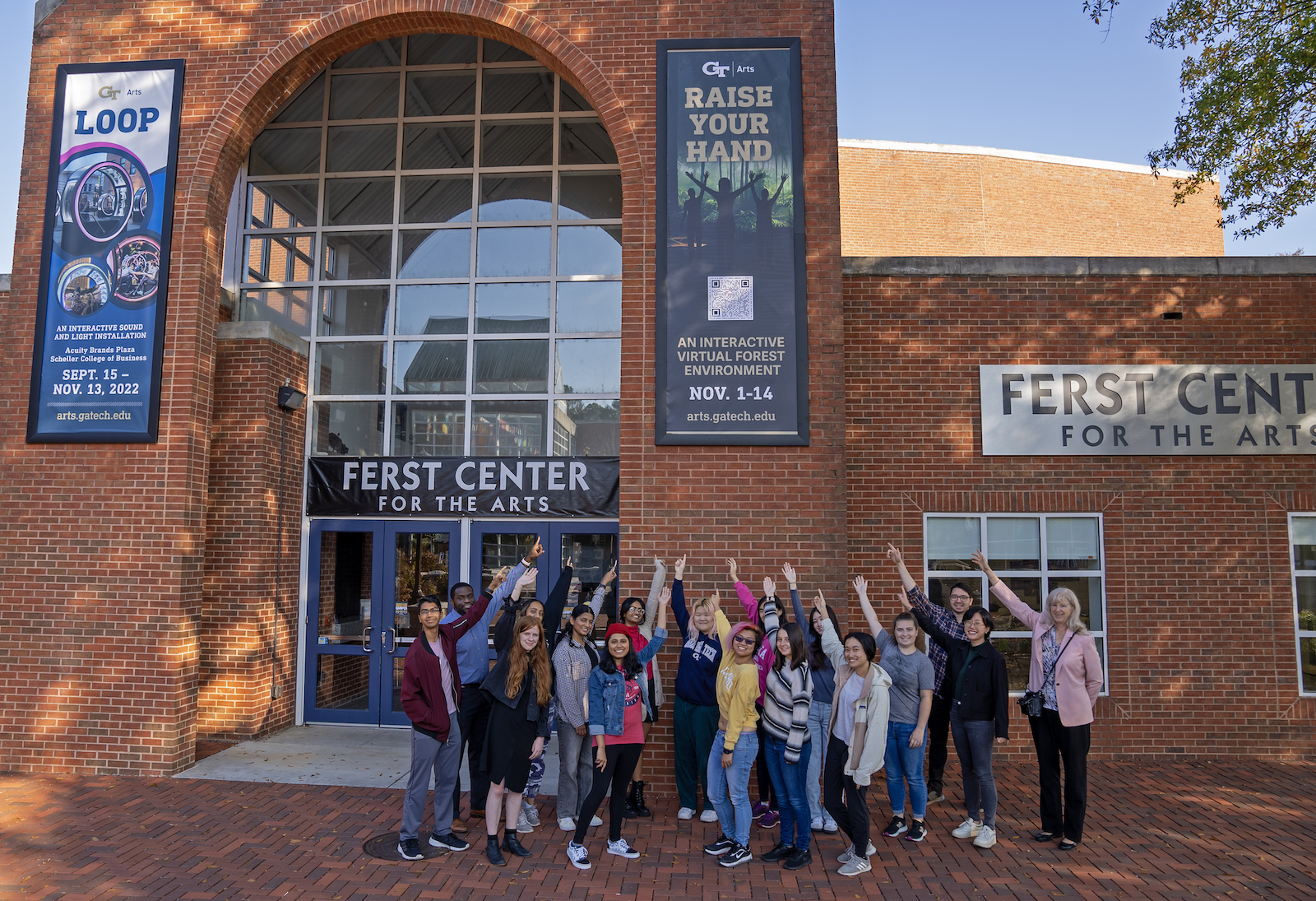 Students and faculty at the Ferst Center for the Arts, pointing at a sign for "Raise Your Hand."