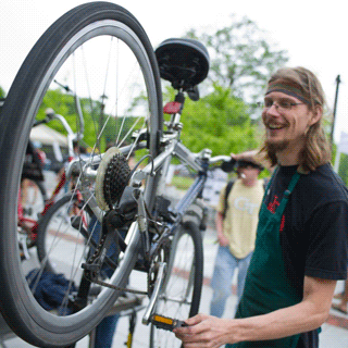 A smiling male Tech student works on a bicycle.