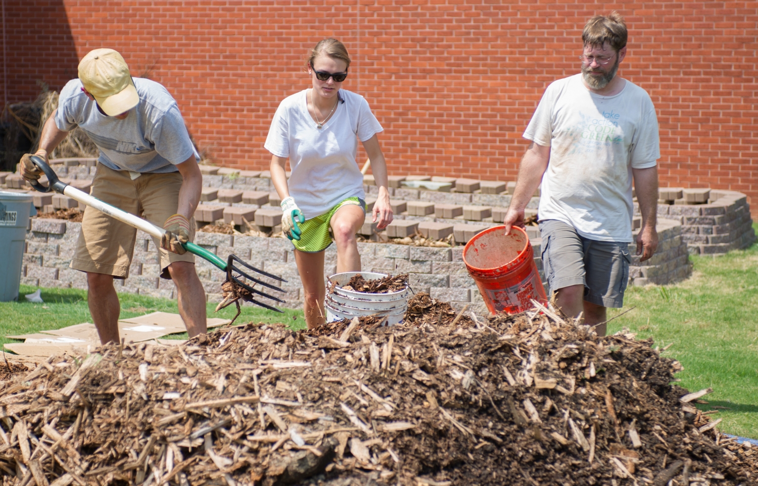 Students and staff spread mulch at the campus community garden in August 2013