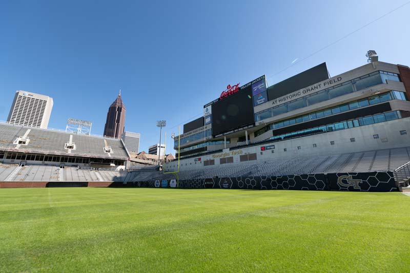 A sunny day at Grant Field, with an expanse of green grass and football stadium stands around it