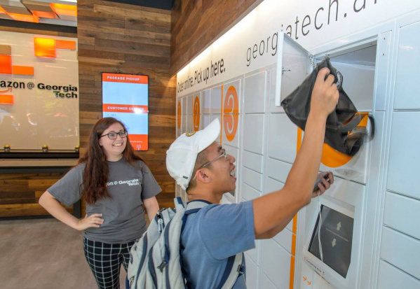 Inside the Amazon pickup location at Georgia Tech, a student removes an item from a locker while an Amazon employee looks on