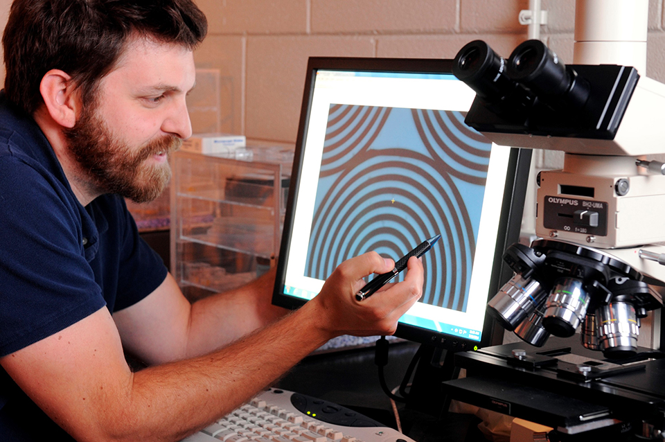 GTRI researcher Stephan Turano shows an optical microscope image of one of the carbon nanotube array patterns on a solar cell shown on a computer screen. The solar cell will be tested on the International Space Station.
