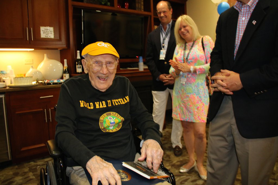 Chester Gryzbowski wearing a RAT cap and a U.S. Army sweatshirt, sitting in a wheelchair, surrounded by family members