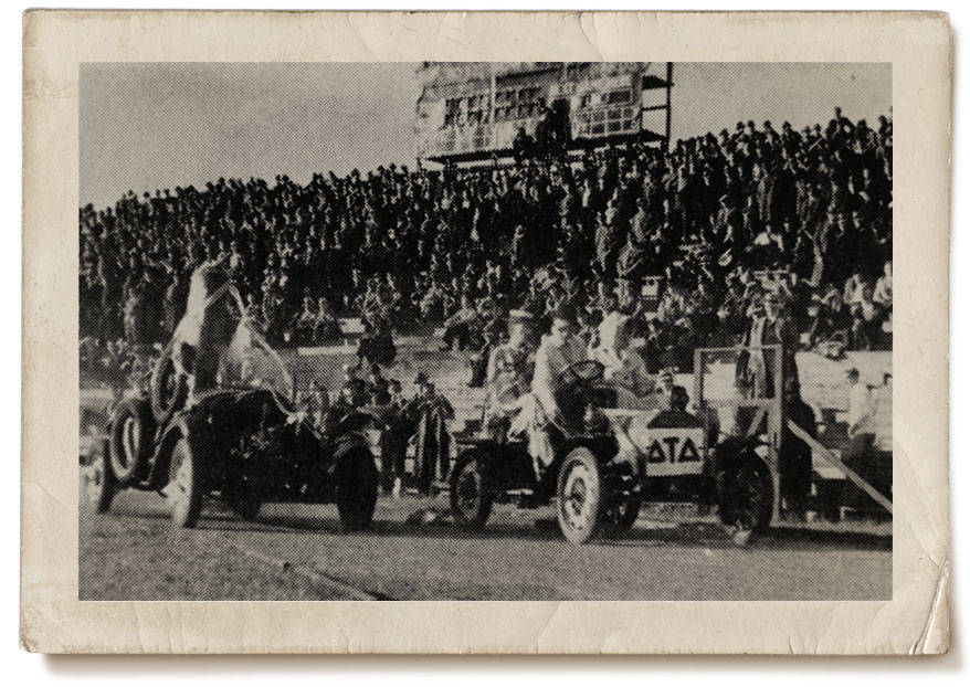Proud Georgia Tech students cruising in the 1932 Ramblin' Wreck Parade in what appears to be a stadium with a crowd of onlookers on riser seating..