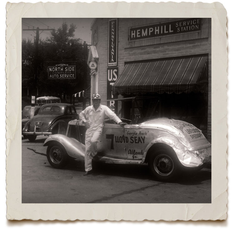 Lloyd Seay standing against his shiney but banged up racecar at Hemphill Station