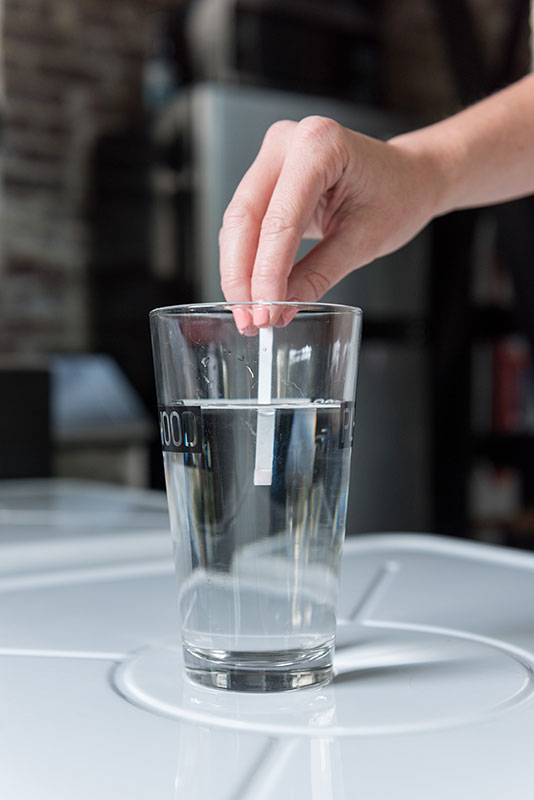 A closeup of a water glass with a test strip being dipped into it