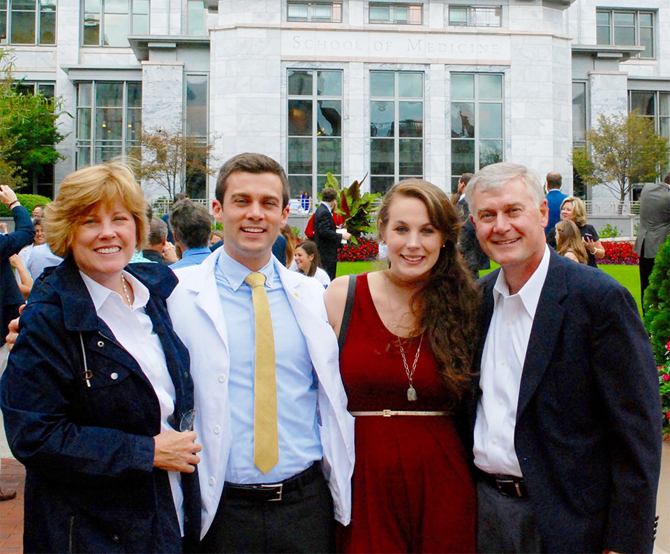 Chris Hauser, wearing a white doctor's coat, with his family, outside the Emory School of Medicine