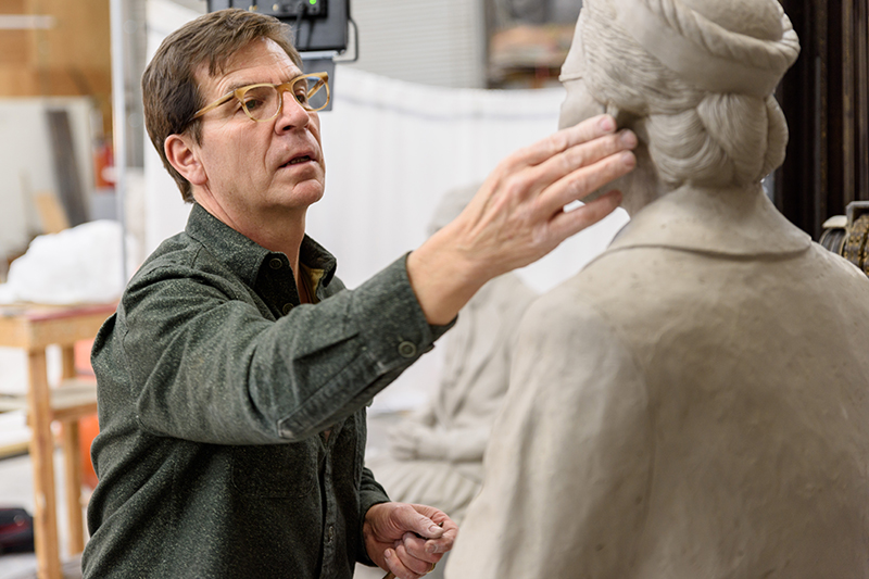 Close up of sculptor as he adjusts a detail on the head of one of the sculptures