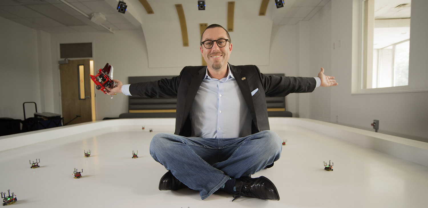 Magnus Egerstedt sitting in the Robotarium in the robot pool, spreading his arms to show off the space.