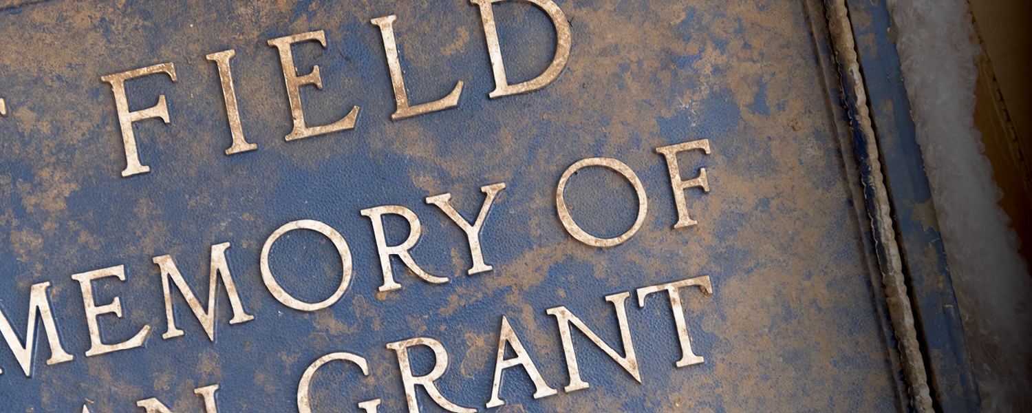 A closeup of a plaque, covered in dirt, that has an inscription dedicated to Hugh Inman Grant
