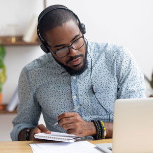 A man wearing headphones and taking notes at his computer