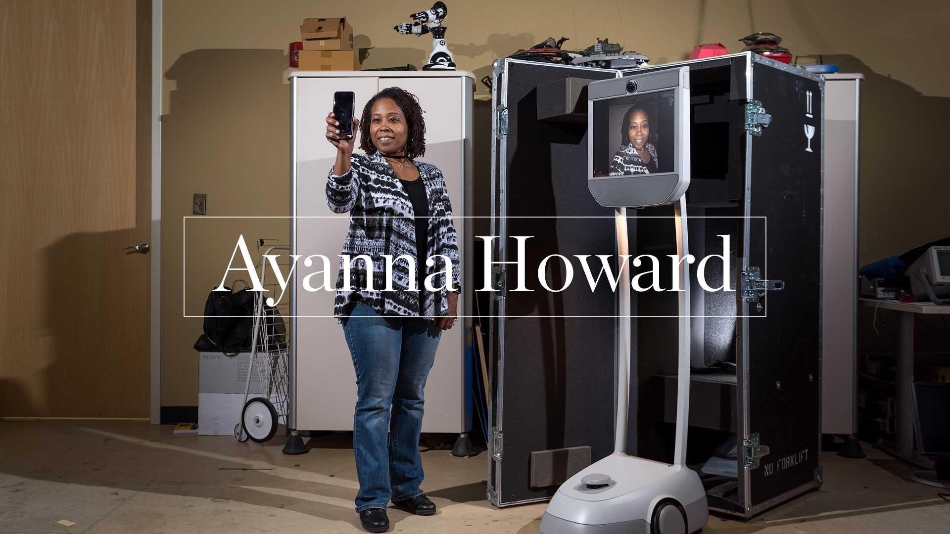 photo - Ayanna Howard holding up smartphone with her image appearing on face of robot