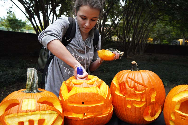 A student lighting a carved jack o'lantern with others on the table