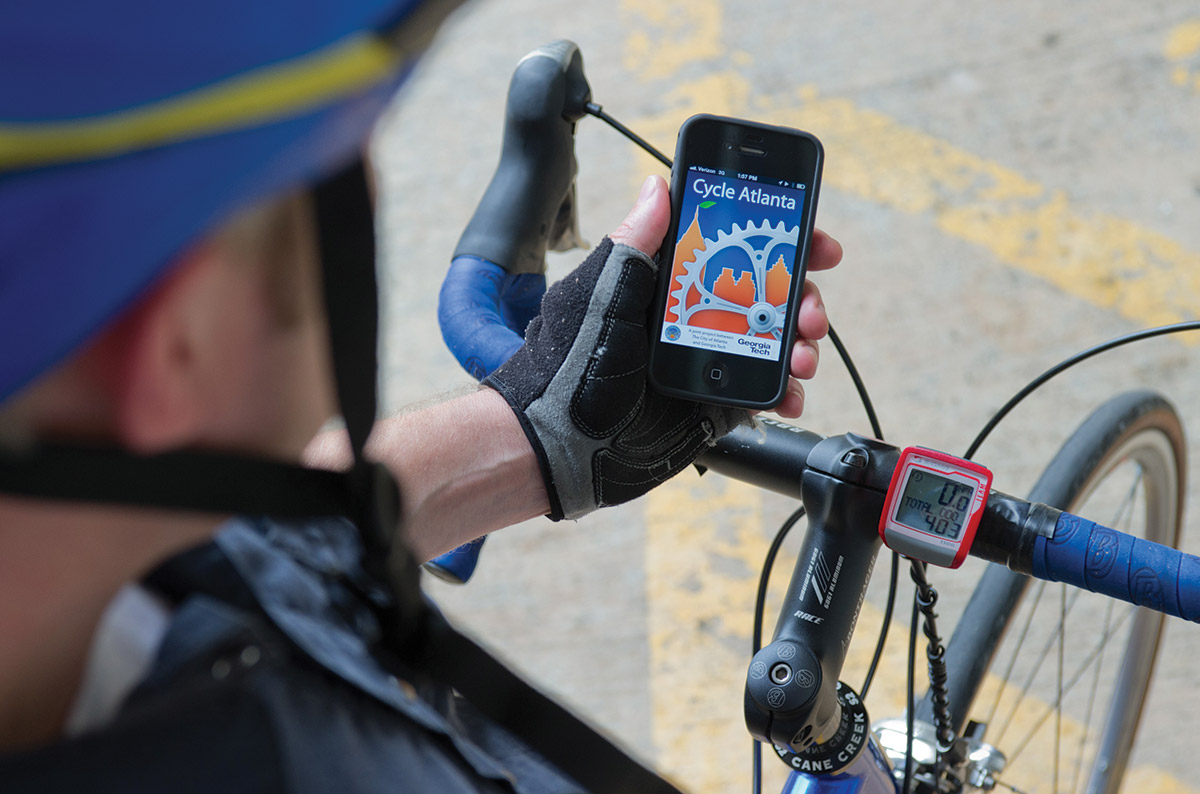 Man in cycling gear and riding a bike holds a cell phone displaying an app called Cycle Atlanta