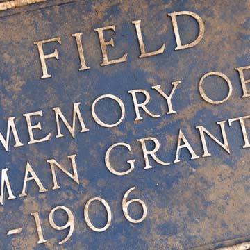 A closeup of a plaque, covered in dirt, that has an inscription dedicated to Hugh Inman Grant