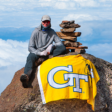 Sam Chaneles stands on top of a mountain holding a Georgia Tech flag.
