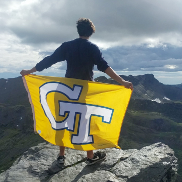 Georgia Tech student holds a GT flag on a mountaintop