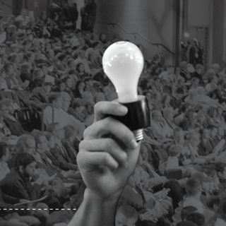 A hand holds up a light bulb in the crowd of people watching the Inventure Prize competition.