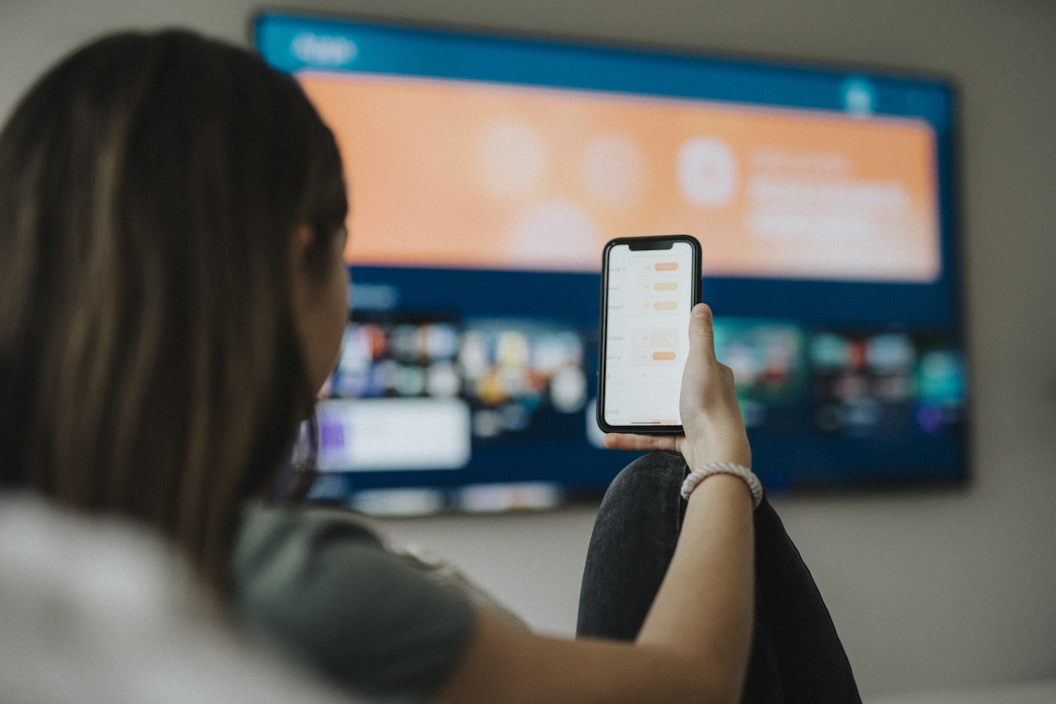 Woman watching TV while scrolling on phone. 