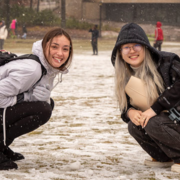 Two students kneeling in snow
