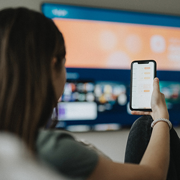 Woman watching TV while scrolling on phone. 