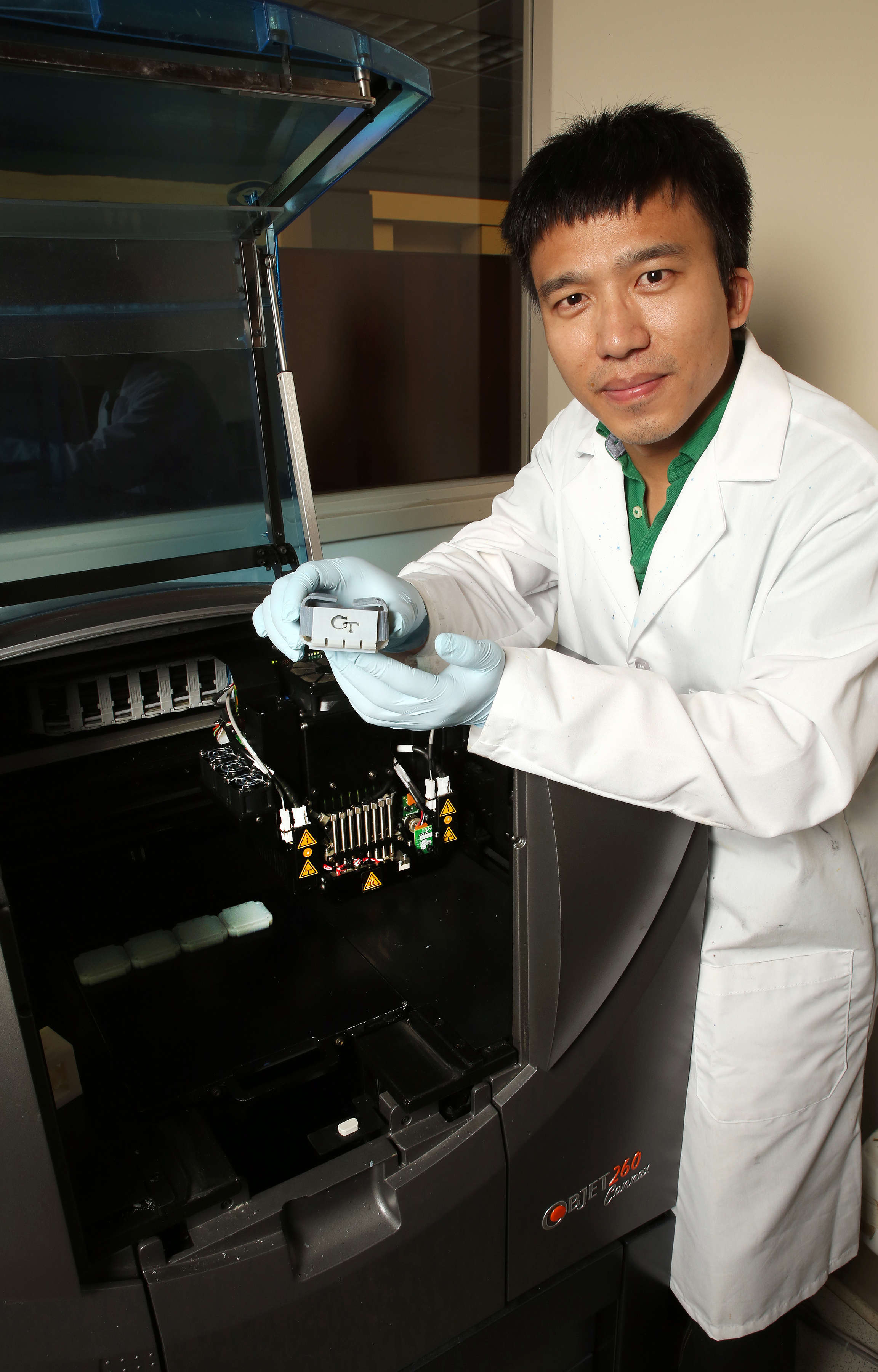 Yiqi Mao, a postdoctoral fellow in the laboratory of Professor Jerry Qi at Georgia Tech, shows a folded box structure produced from smart shape-memory materials. The materials were created with the 3-D printer shown with him. (Credit: Candler Hobbs, Georgia Tech)