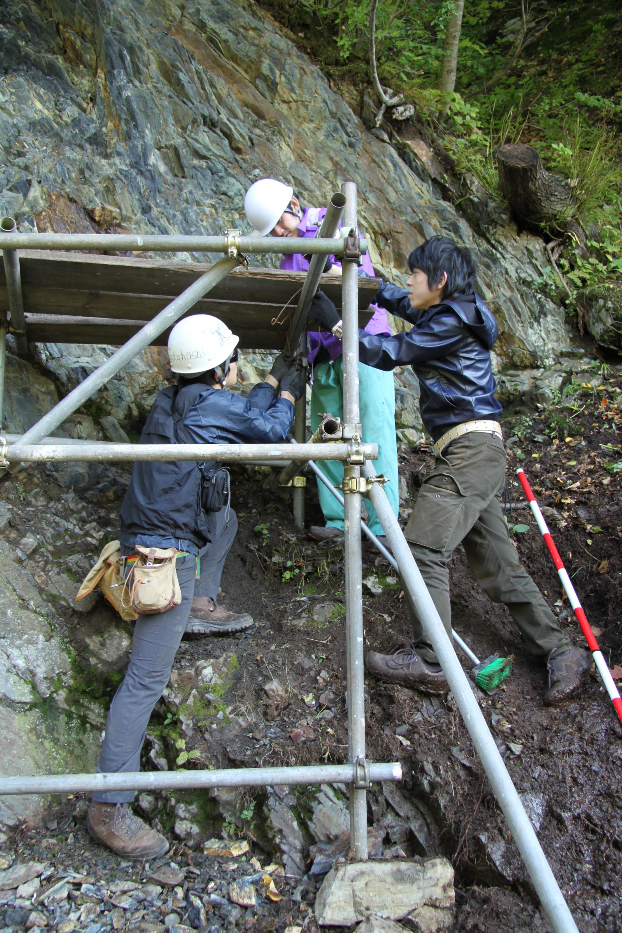 First author Kazumi Ozaki (r.) takes geological samples from layers of rock formed during the Great Permian Extinction. He is shown here with other researchers in Japan doing work unrelated to this study.  Credit: Satoshi Takahashi / University of Tokyo