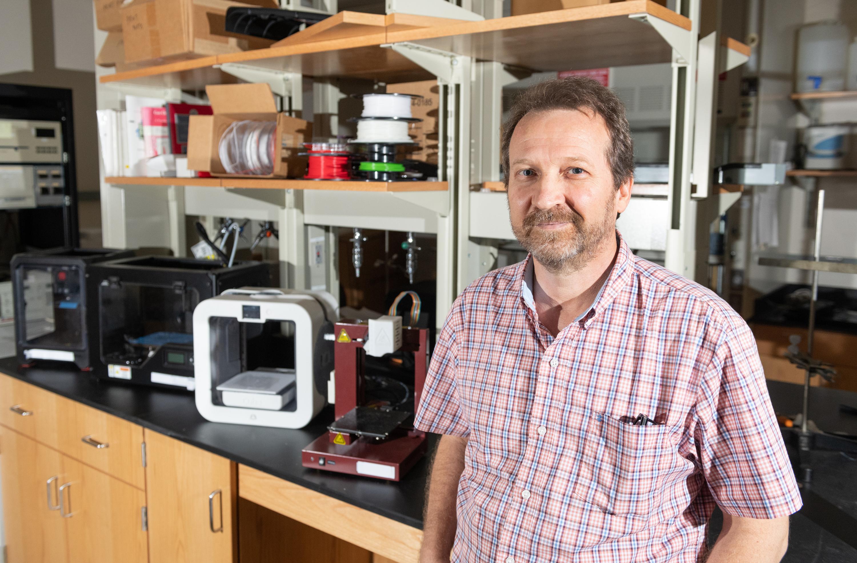 Rodney Weber, a professor in Georgia Tech’s School of Earth & Atmospheric Sciences, stands in his lab alongside several consumer-grade 3D printers. (Credit: Allison Carter)