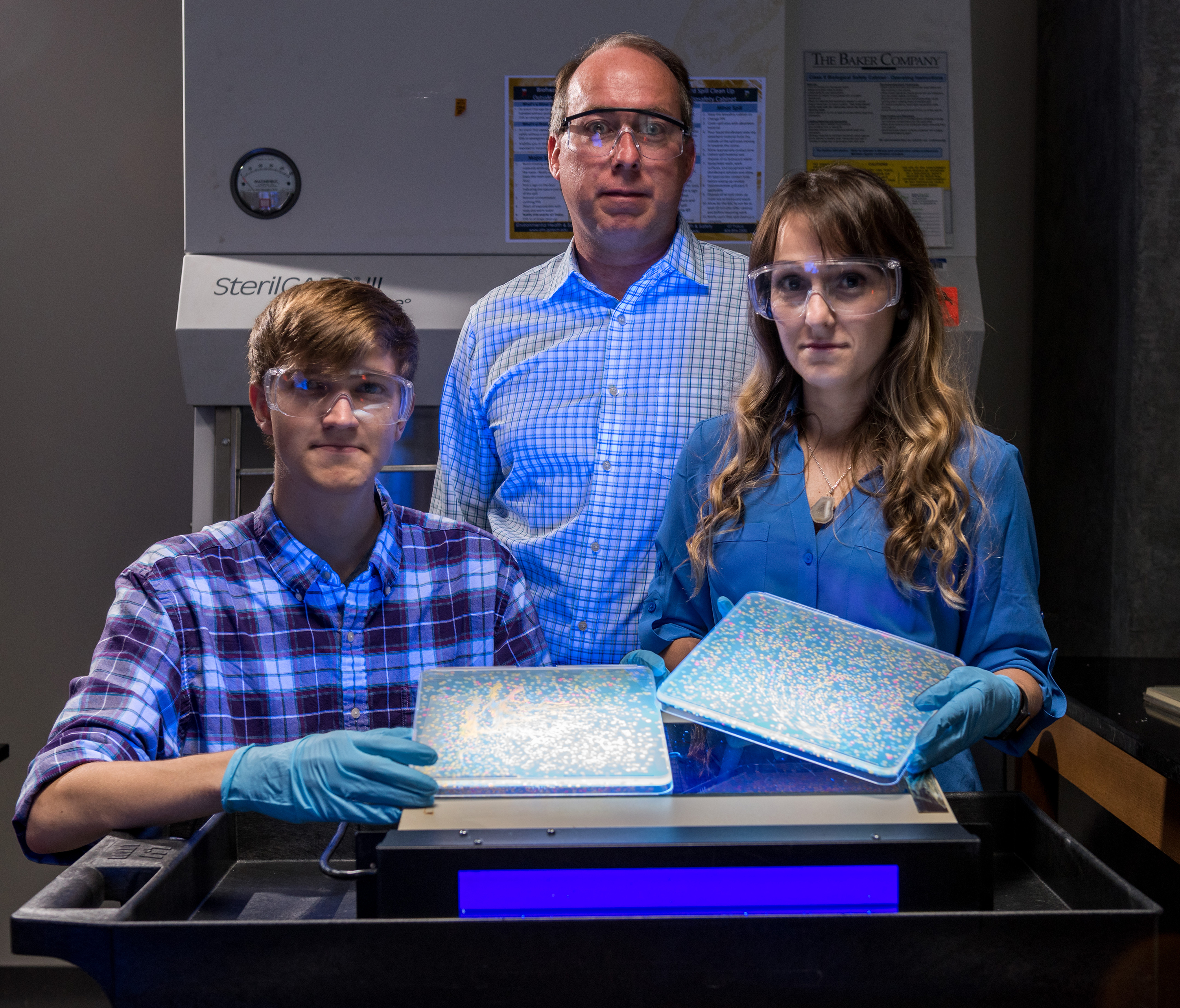 Eric Gaucher (center) and researchers in his lab, Caelan Radford (left) and Ryan Randall hold samples of bacteria with an array of mutated proteins that fluoresce in different colors. Credit: Georgia Tech / Rob Felt