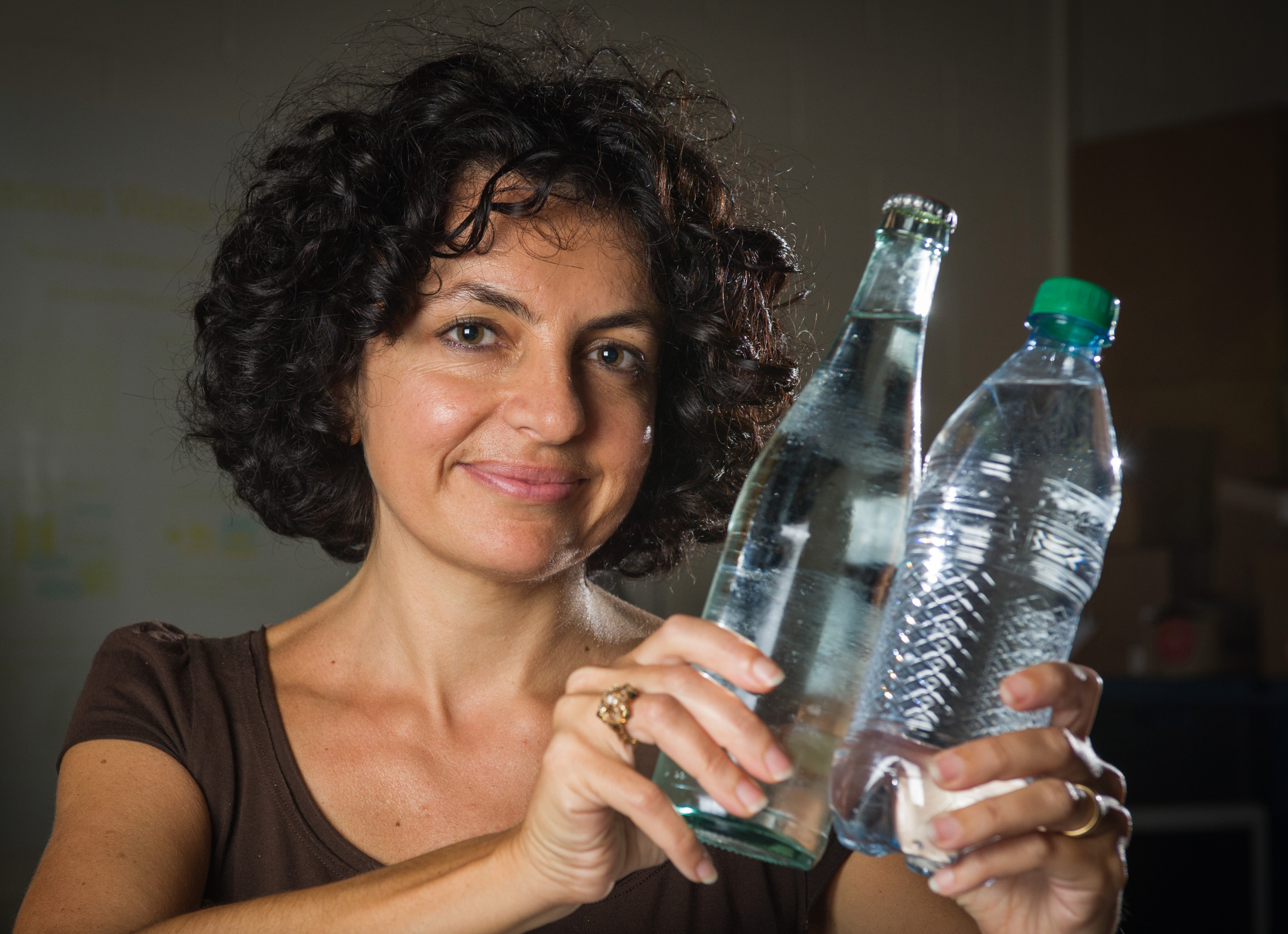 Georgia Tech School of Physics associate professor Elisa Riedo poses with a glass water bottle and a plastic water bottle. While container materials don’t significantly affect the rate at which water pours from bottles of this size, a new study shows that the properties of containers at the nanoscale dramatically affect the viscosity of water. (Georgia Tech Photo: Rob Felt)
