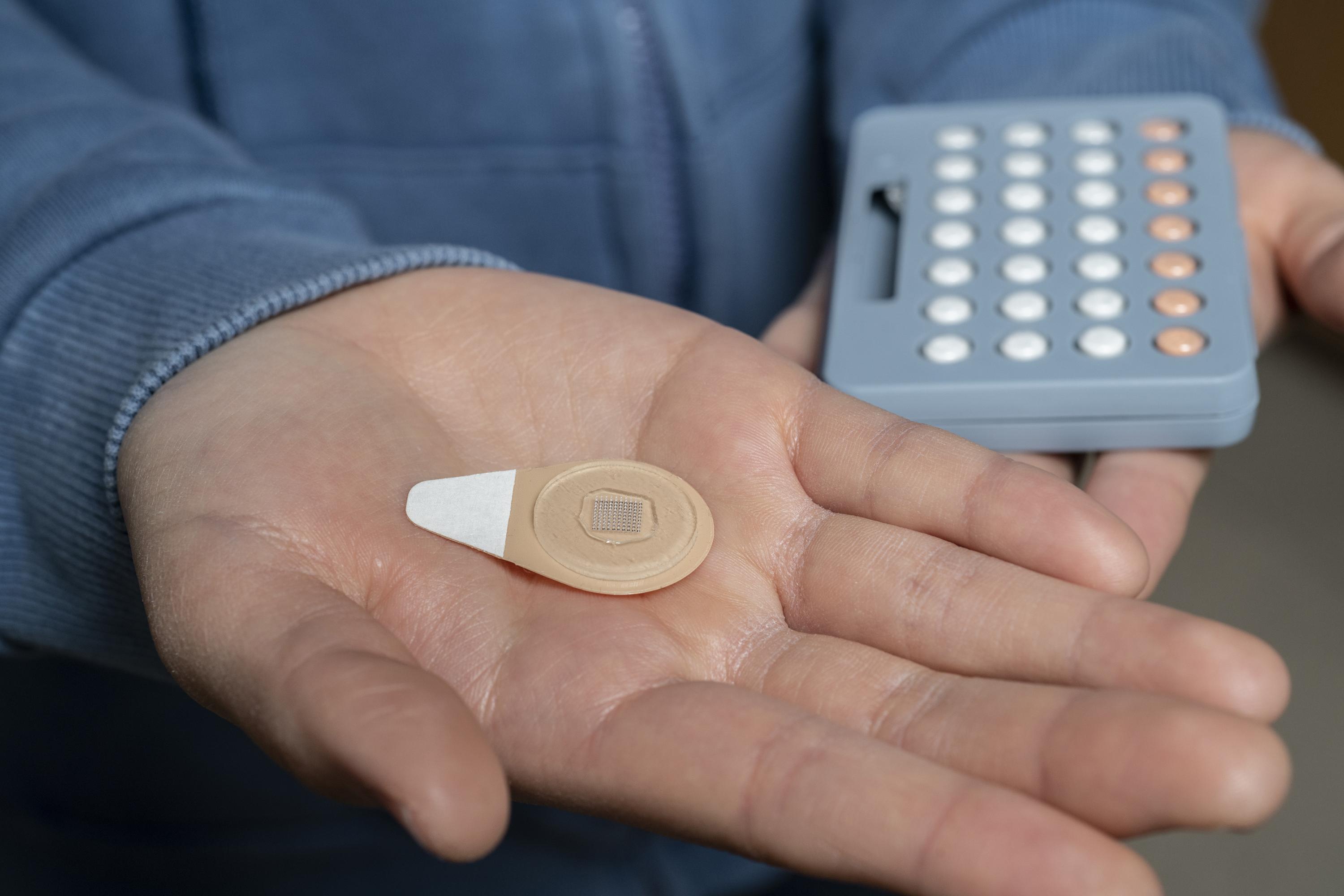 An experimental microneedle patch is shown next to a blister pack of birth control pills. Designed to be self-administered by women for long-acting contraception, the patch could provide a new family planning option. (Credit: Christopher Moore, Georgia Tech)