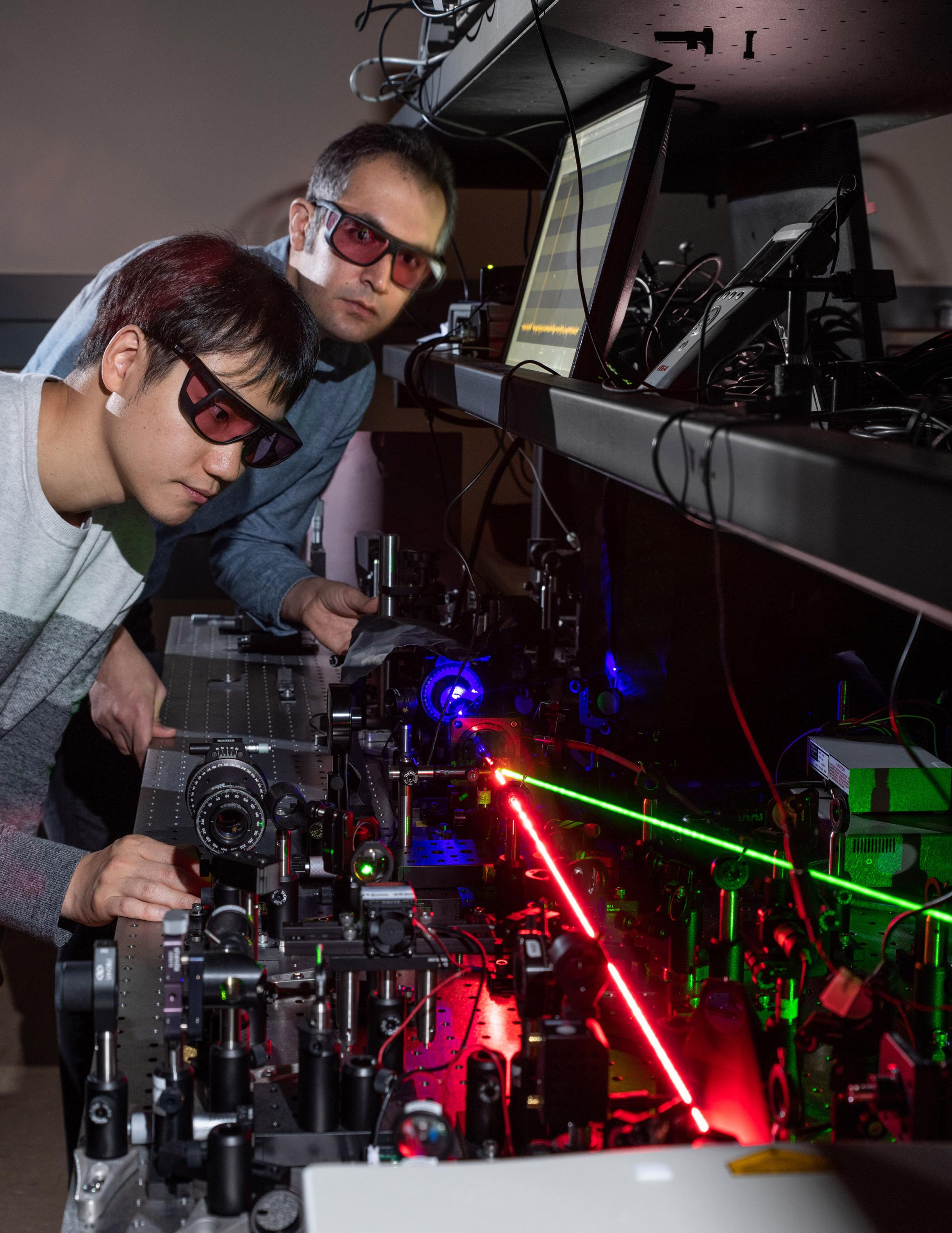 Georgia Tech researchers Kyu-Tae Lee and Mohammad Taghinejad demonstrate frequency doubling on a slab of titanium dioxide using a red laser to create nonlinear effects with tiny triangles of gold. The blue beam shows the frequency-doubled light and the green beam controls the hot-electron migration. (Credit: Rob Felt, Georgia Tech)