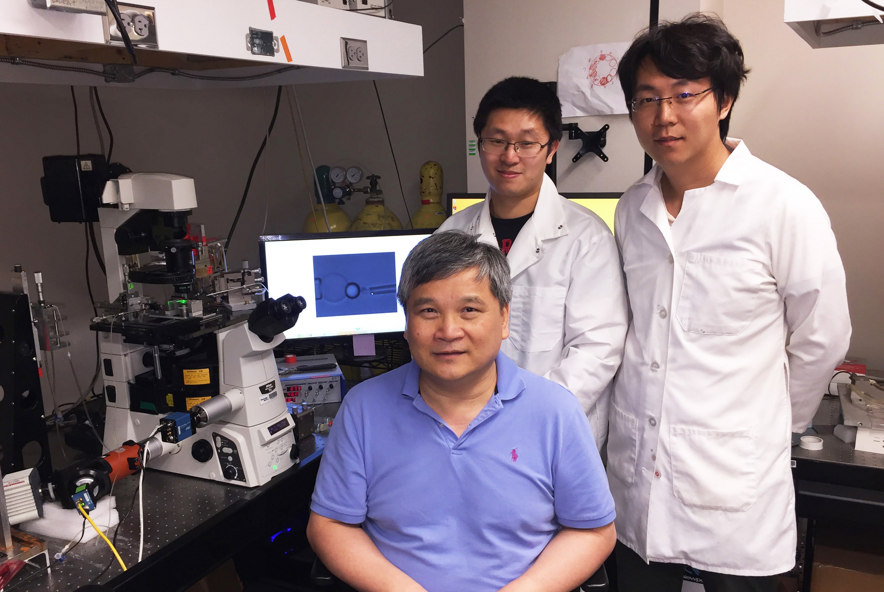 Researchers Lining (Arnold) Ju, Cheng Zhu (seated) and Yunfeng Chen are shown with the single-molecule force measurement tool used to study how platelets sense the mechanical forces they encounter during bleeding. (Credit: John Toon, Georgia Tech)