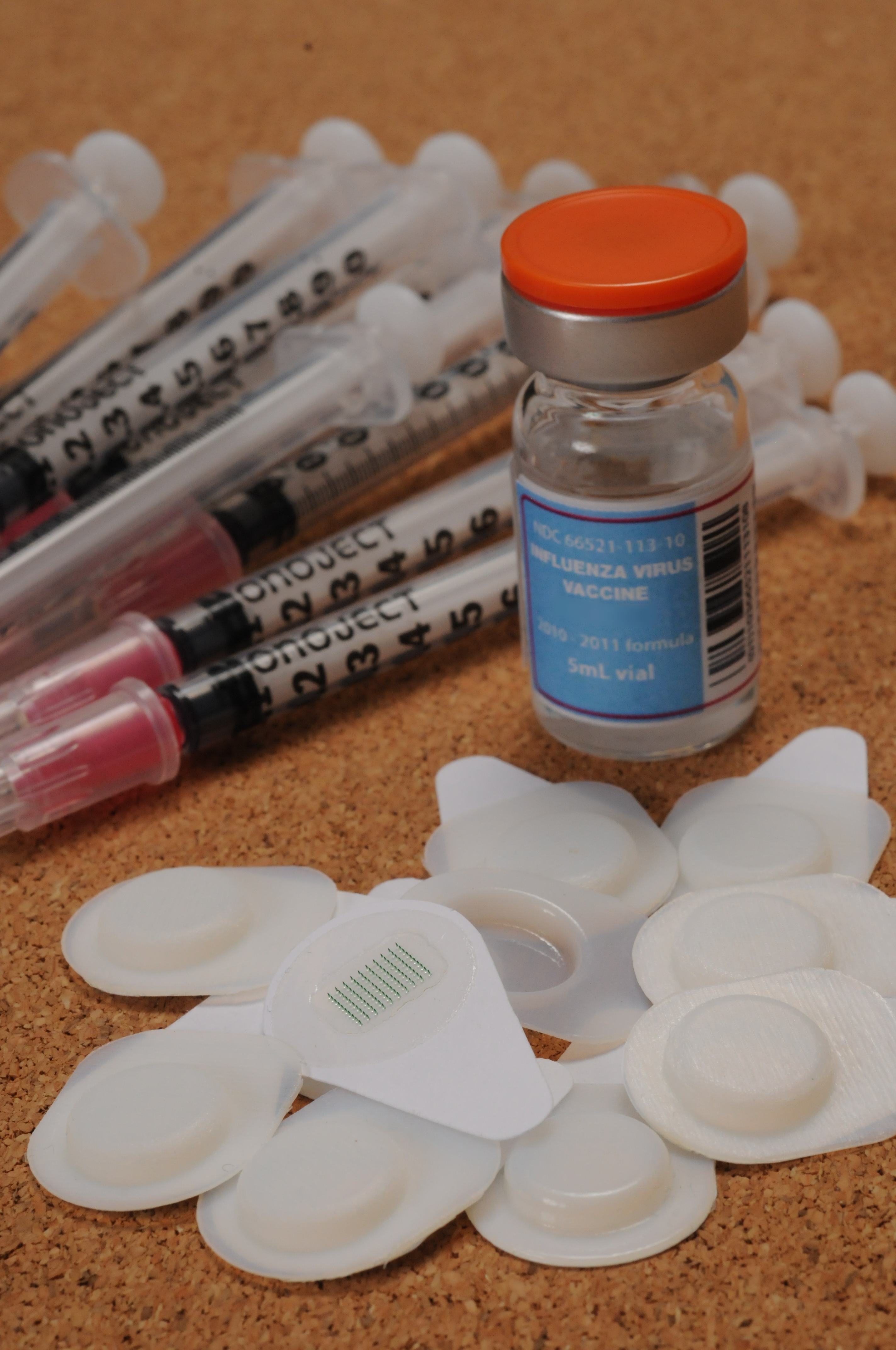 Ten microneedle patches are shown with a ten-dose vial of influenza vaccine and ten hypodermic needles with syringes. (Georgia Tech Photo: Gary Meek)