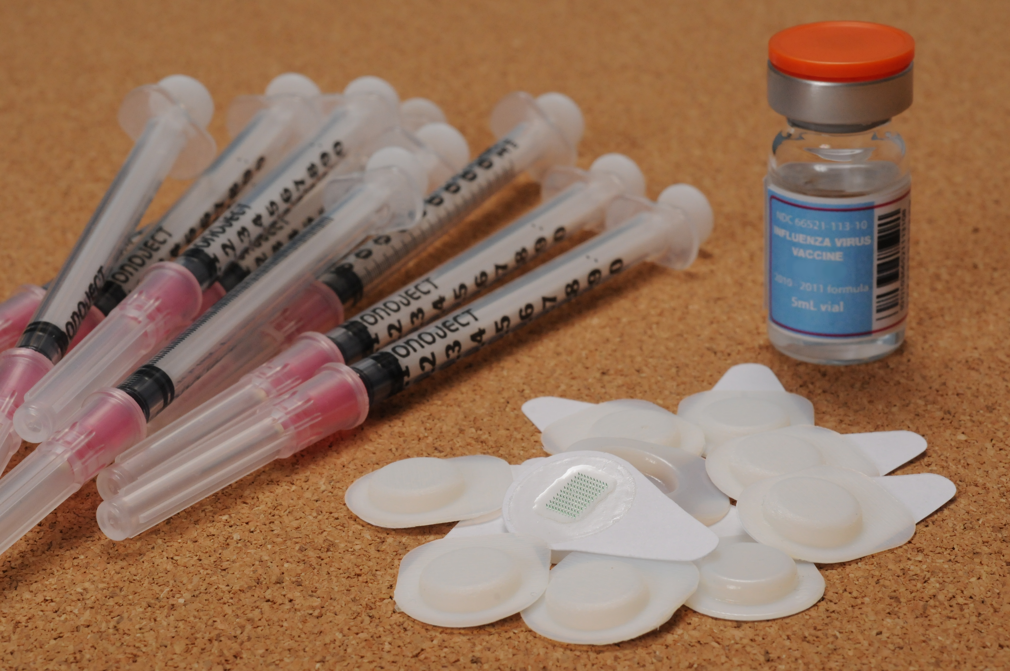 Ten microneedle patches are shown with a ten-dose vial of influenza vaccine and ten hypodermic needles with syringes. (Georgia Tech Photo: Gary Meek)
