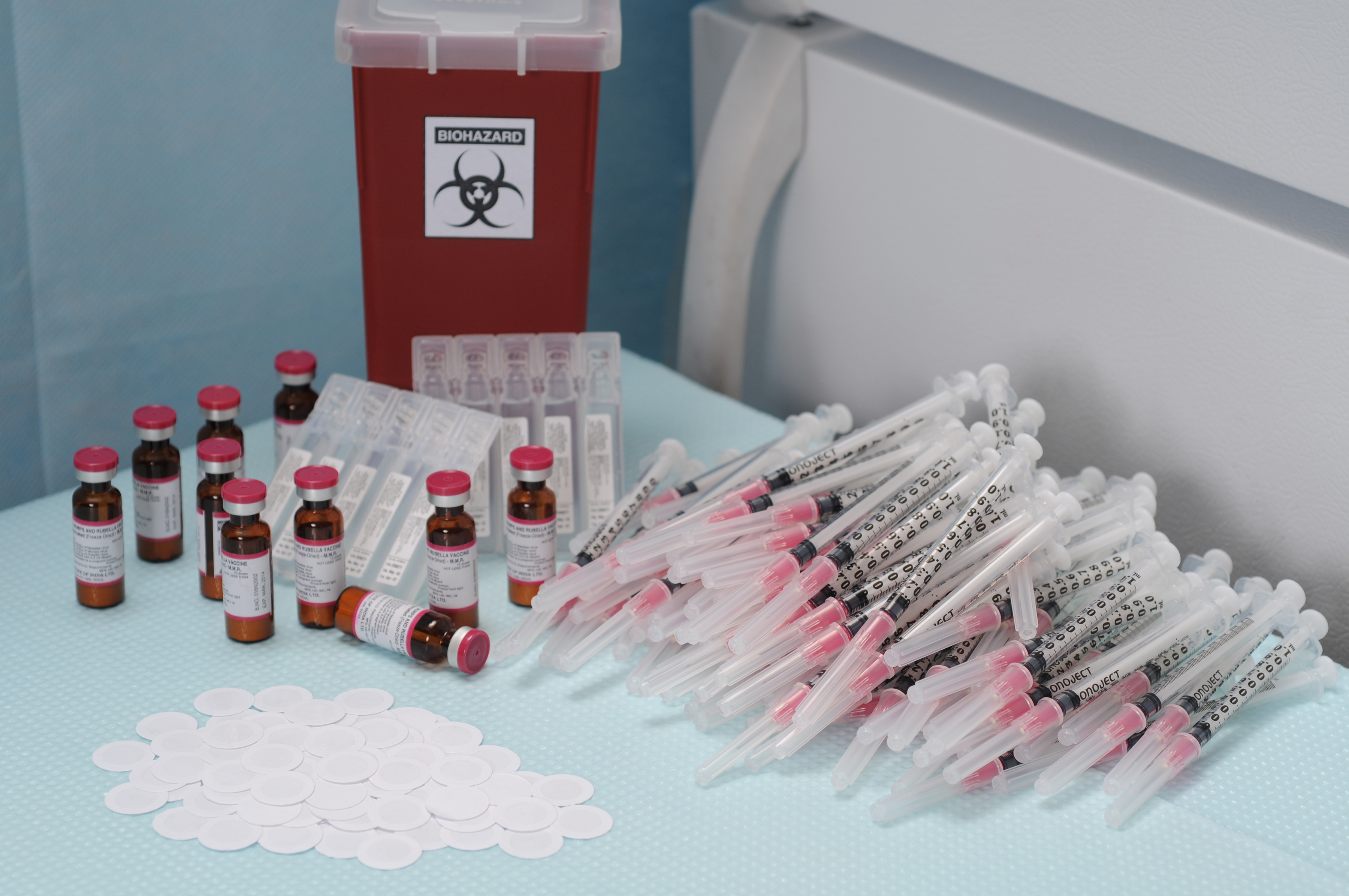 The 100 microneedle patches (white) in the foreground could replace everything in the background: the 100 needles and syringes, 10 ten-dose vials of measles vaccine with diluent, a biohazards box for sharps waste disposal, and a refrigerator for cold chain storage. (Photo: Gary Meek)