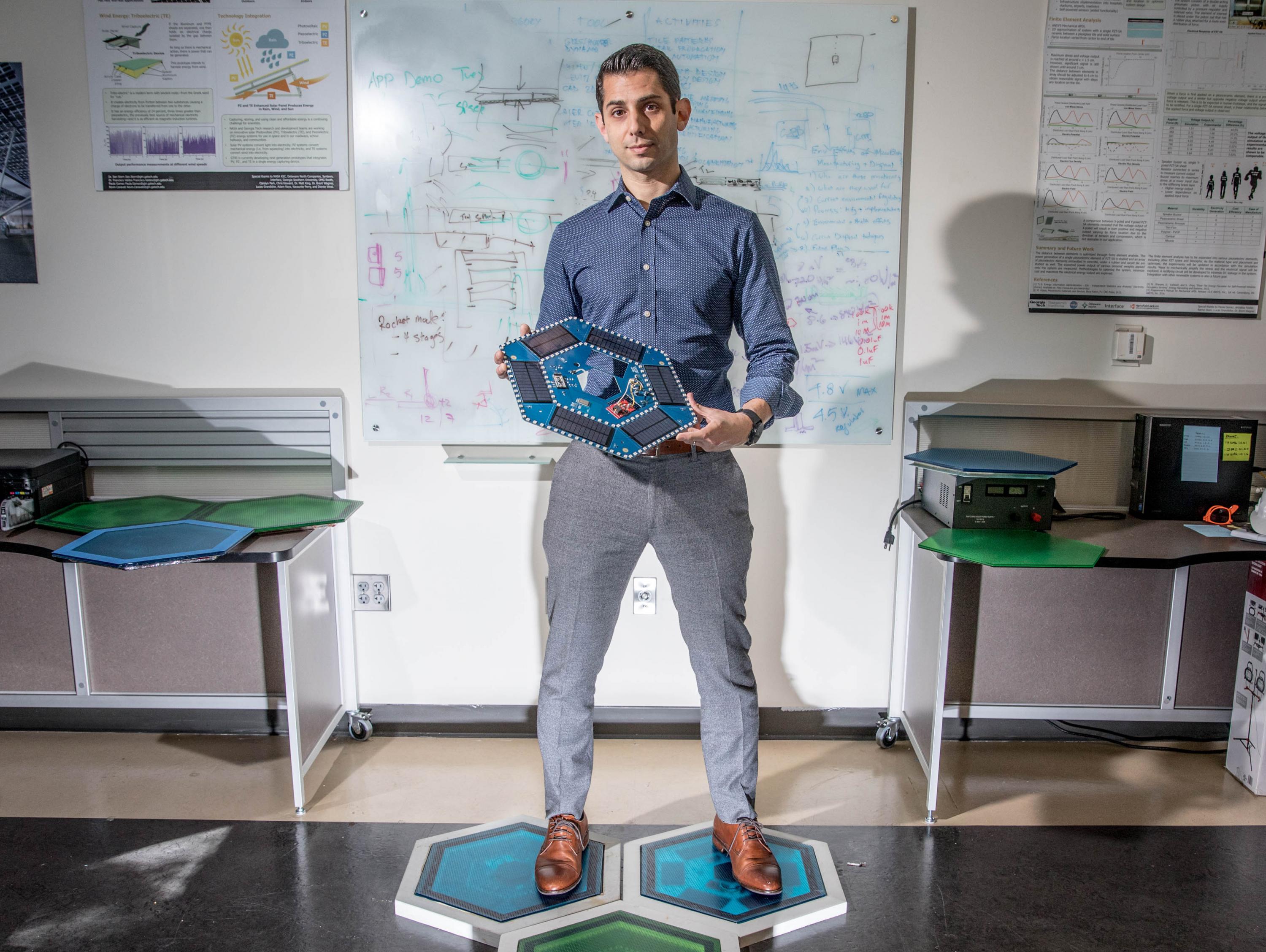 Ilan Stern, a GTRI senior research scientist, stands on piezoelectric tiles that will be used to create a lighted outdoor footpath at the NASA Kennedy Space Center’s Visitor Complex at Cape Canaveral, Florida. He’s holding the electronic components used in the tiles. (Credit: Branden Camp, Georgia Tech)