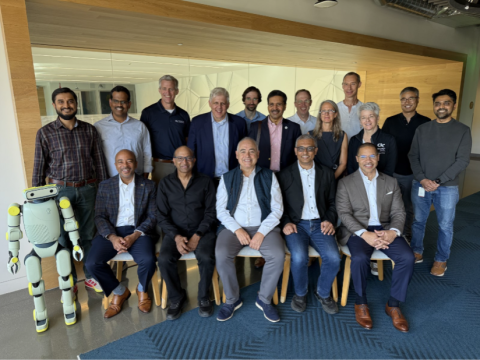 Image shows a small humanoid robot standing beside 5 men who are seated, with GT President Cabrera in the middle, wearing a blue vest. Behind the seated group are 12 people standing, including 2 women.