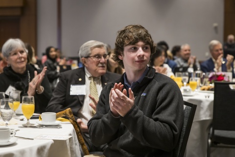 Student clapping in the foreground at a table with donors sitting behind him