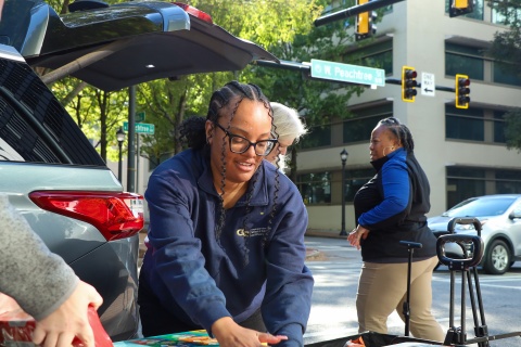 A smiling woman unloading food from a car. 