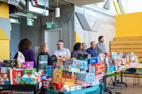 A group of people standing around a large amount of food for Klemis Kitchen. 