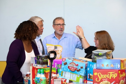 A group of people standing around a large amount of food for Klemis Kitchen. 