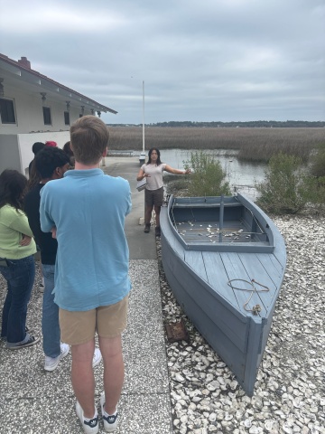 A group of students standing by a wooden rowboat.