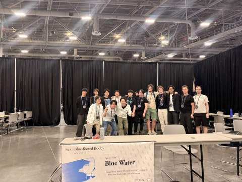 A group of people standing inside of a convention hall. Their banner has their team name, Blue Water