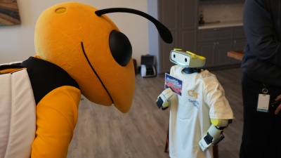Photo of Buzz the mascot leaning down toward a small humanoid robot wearing a Georgia Tech t-shirt