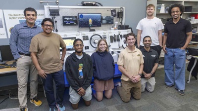 A group photo of students and faculty standing around lab equipment found on a ship. 