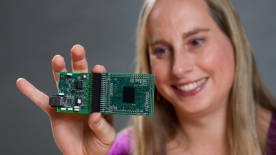 Professor Jennifer Hasler displays a field programmable analog array (FPAA) board that includes an integrated circuit with biological-based neuron structures for power-efficient calculation.  Hasler’s research indicates that this type of board, which is programmable but has low power requirements, could play an important role in advancing neuromorphic computing. (Georgia Tech Photo: Rob Felt)